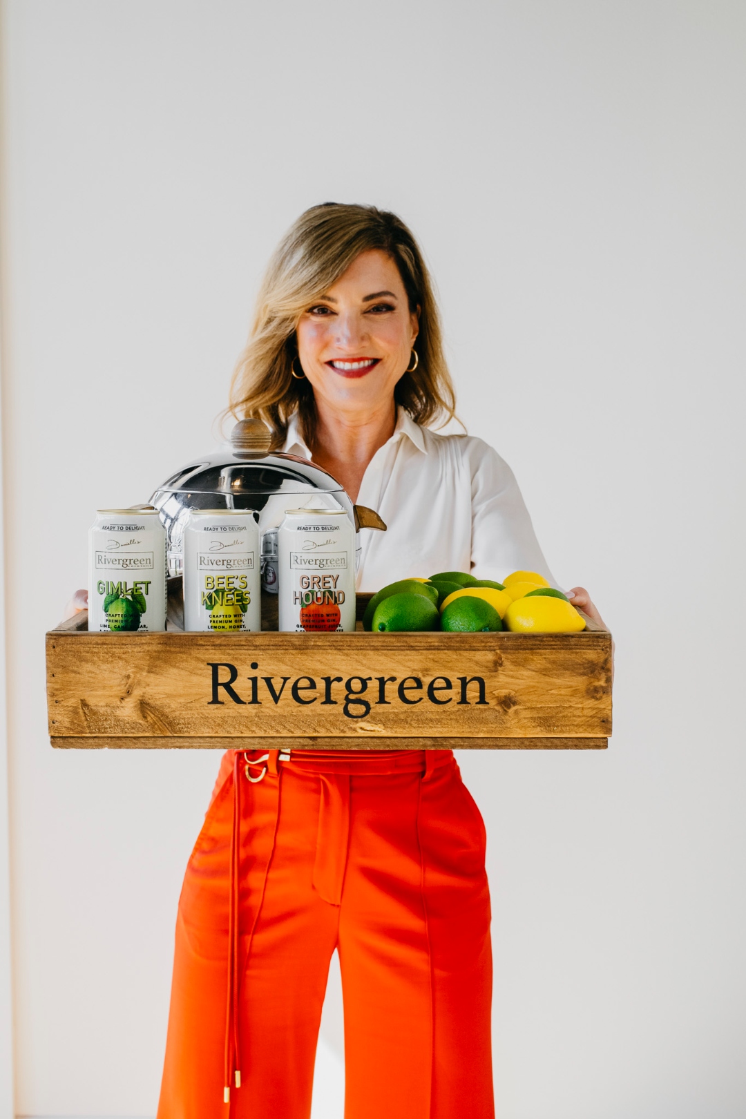 Danielle, Founder and CEO of Rivergreen Cocktails, holding a tray of products and fresh citrus